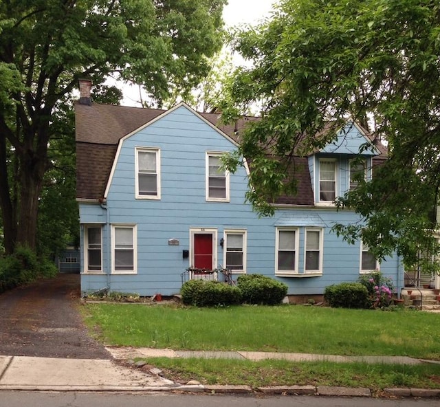 view of front of home with a shingled roof, a chimney, a front yard, and a gambrel roof