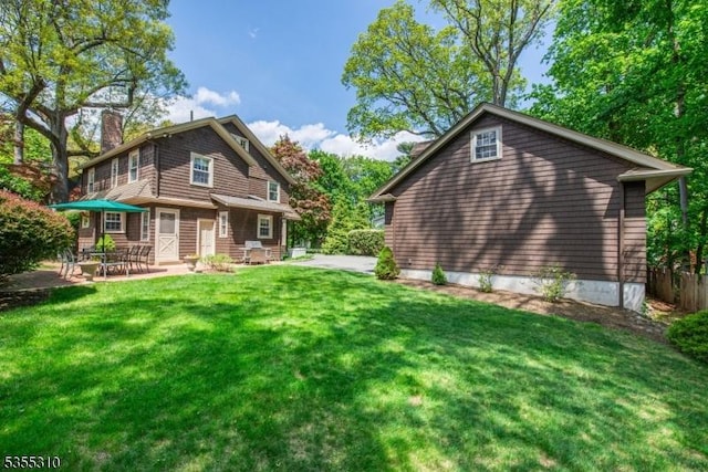 back of house with a chimney, a patio, and a lawn