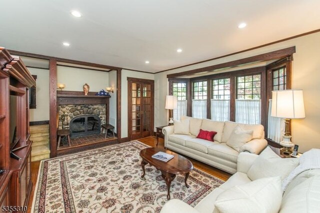 living room featuring wood finished floors, recessed lighting, crown molding, a stone fireplace, and french doors