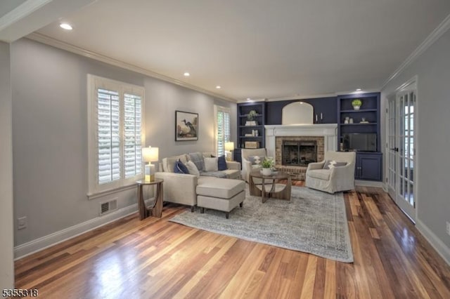 living room with crown molding, visible vents, wood finished floors, a fireplace, and built in shelves