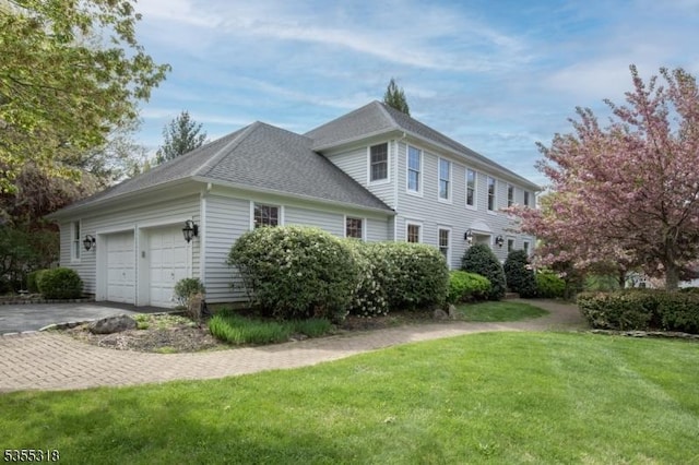 view of property exterior featuring roof with shingles, an attached garage, a yard, and aphalt driveway