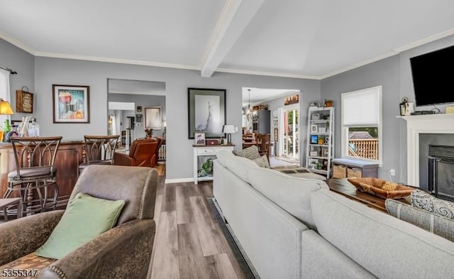 living area with baseboards, ornamental molding, a glass covered fireplace, wood finished floors, and beamed ceiling