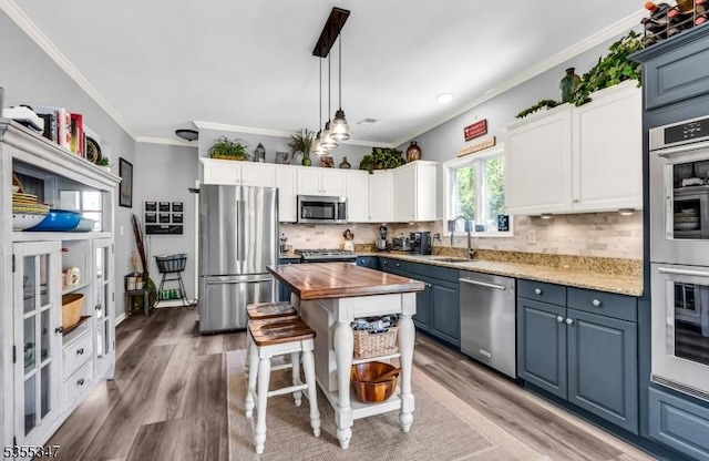 kitchen with wood finished floors, a sink, stainless steel appliances, crown molding, and butcher block counters
