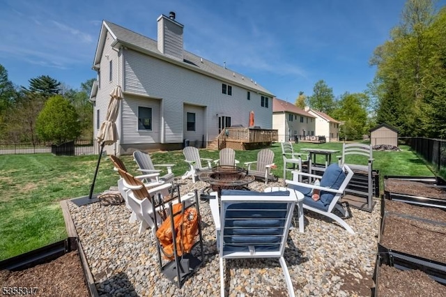 rear view of house with a chimney, a lawn, fence, a fire pit, and a storage unit