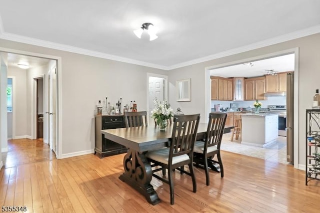 dining room featuring light wood-type flooring, crown molding, and baseboards