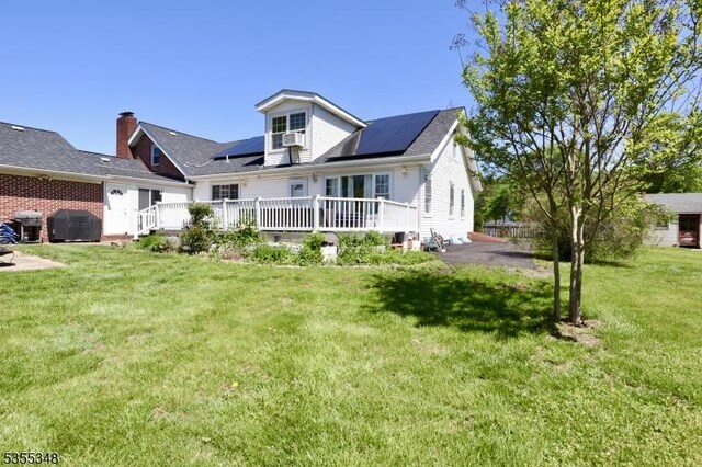 back of property featuring roof mounted solar panels, a deck, and a yard