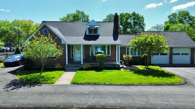 new england style home with asphalt driveway, a front yard, brick siding, a chimney, and a porch