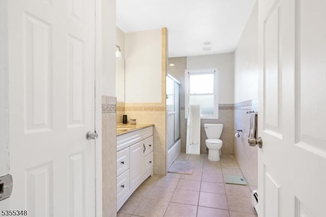 full bath with tile walls, tile patterned flooring, toilet, vanity, and a wainscoted wall