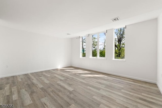 spare room with baseboards, visible vents, and wood finished floors