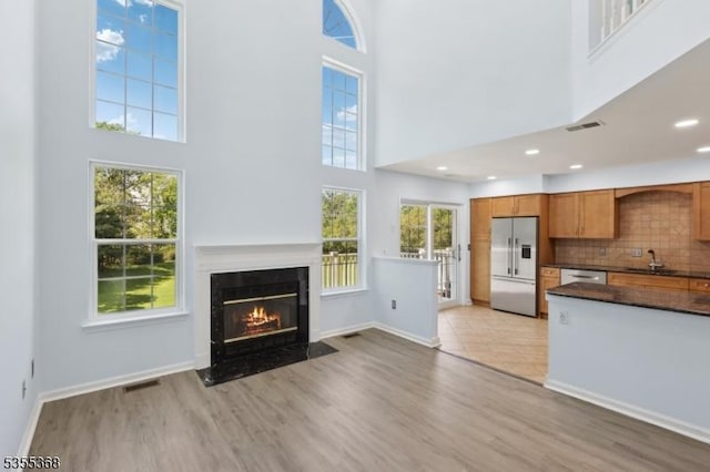 4703 Patterson St, Bridgewater Twp, NJ 08807 - unfurnished living room featuring light wood-style floors, a towering ceiling, baseboards, a fireplace with flush hearth, and a sink