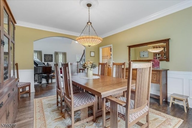 dining space featuring arched walkways, wood finished floors, ornamental molding, wainscoting, and stairway