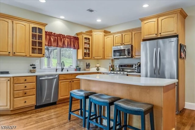 kitchen with stainless steel appliances, a breakfast bar, wood finished floors, glass insert cabinets, and a sink
