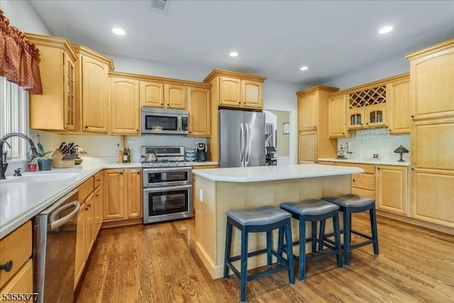 kitchen featuring stainless steel appliances, a sink, a kitchen breakfast bar, light brown cabinetry, and recessed lighting