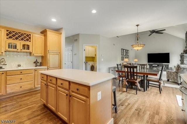 kitchen featuring washer / dryer, light countertops, a kitchen island, glass insert cabinets, and lofted ceiling