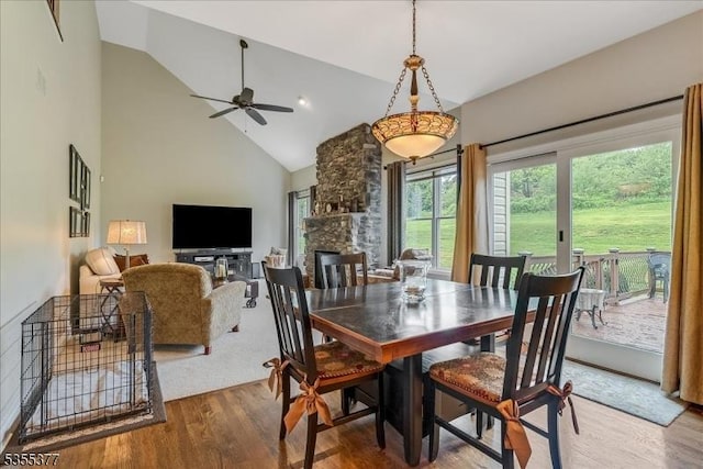 dining room with wood finished floors, high vaulted ceiling, a ceiling fan, and a stone fireplace