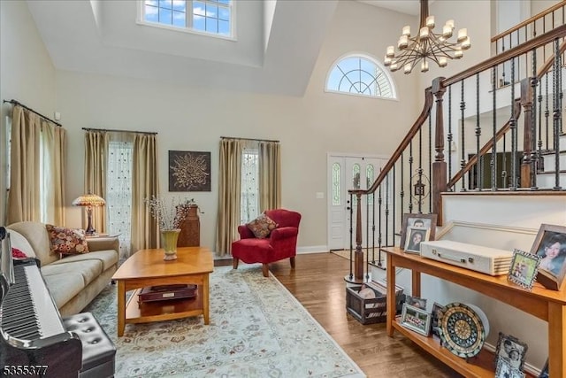 living room featuring a chandelier, a towering ceiling, wood finished floors, stairs, and baseboards