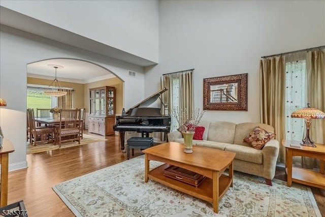 living room featuring arched walkways, light wood finished floors, crown molding, a towering ceiling, and baseboards