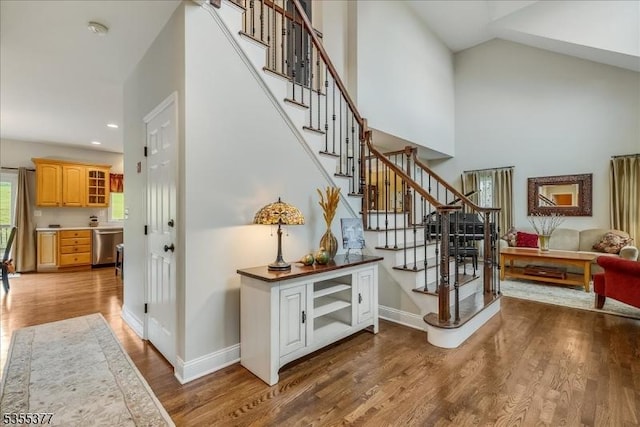 stairway with wood finished floors, baseboards, recessed lighting, and high vaulted ceiling