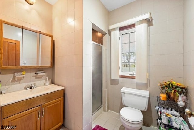 bathroom featuring tile walls, a shower stall, toilet, vanity, and tile patterned flooring