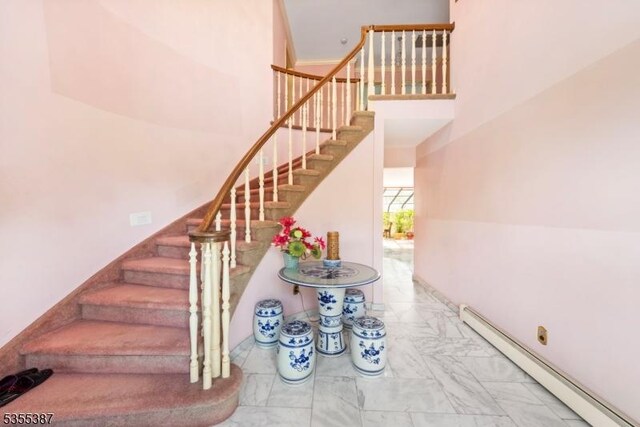 stairway featuring a baseboard radiator, marble look tiles, and a high ceiling