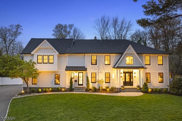 view of front of home featuring a standing seam roof, driveway, roof with shingles, and a front lawn