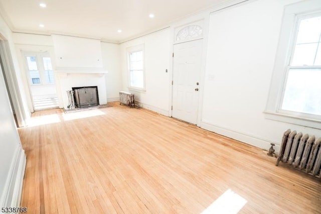 unfurnished living room featuring a fireplace with flush hearth, radiator, and a wealth of natural light