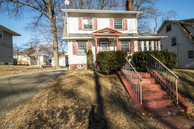 view of front facade featuring a chimney, stairway, and aphalt driveway