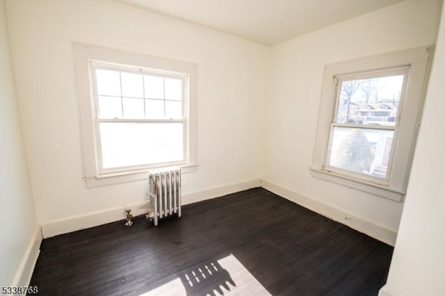 unfurnished room featuring baseboards, dark wood finished floors, and radiator heating unit