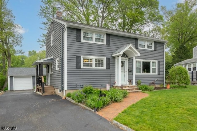 colonial inspired home featuring a chimney, an outdoor structure, asphalt driveway, a front yard, and a detached garage