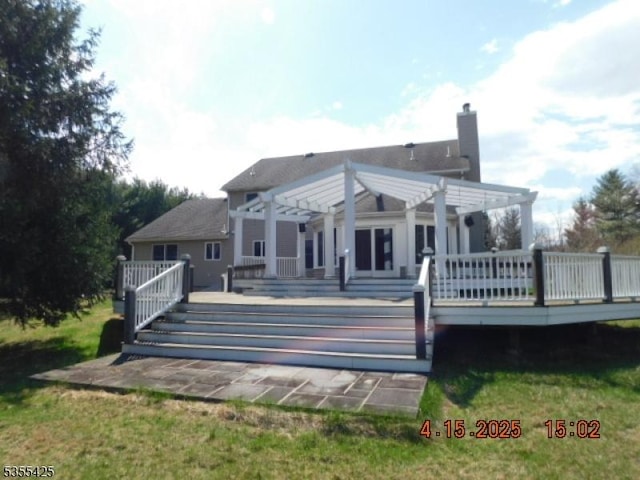 rear view of house featuring a pergola, a wooden deck, and a chimney