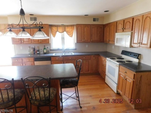 kitchen featuring a sink, white appliances, a breakfast bar area, light wood-type flooring, and visible vents