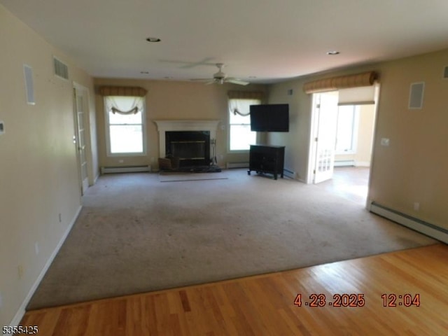 unfurnished living room with ceiling fan, a glass covered fireplace, a wealth of natural light, a baseboard radiator, and visible vents