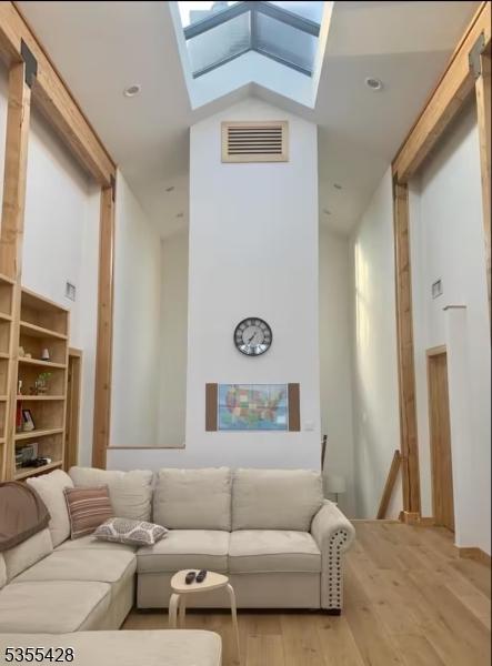 living area with a skylight, high vaulted ceiling, wood finished floors, and visible vents
