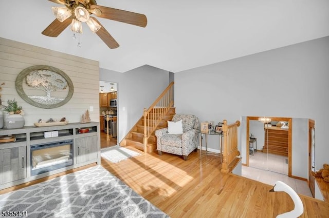living area featuring light wood-type flooring, a ceiling fan, stairs, and baseboards