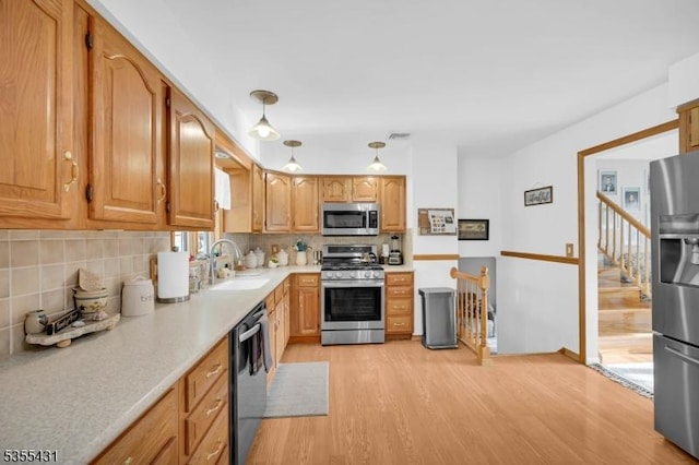 kitchen with stainless steel appliances, a sink, light wood finished floors, and decorative backsplash