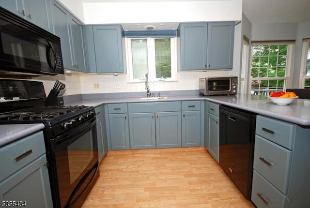 kitchen featuring black appliances, a sink, a peninsula, light wood finished floors, and backsplash