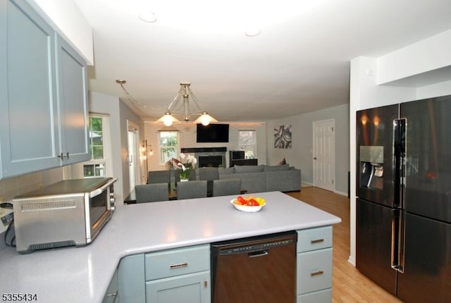 kitchen with black fridge, dishwasher, a peninsula, open floor plan, and a fireplace