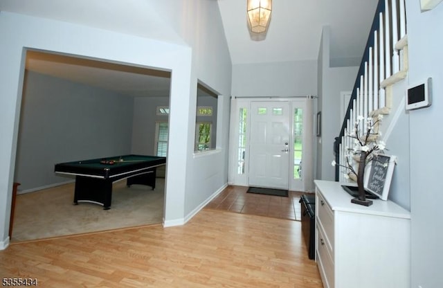 foyer entrance featuring billiards table, stairs, light wood finished floors, baseboards, and high vaulted ceiling