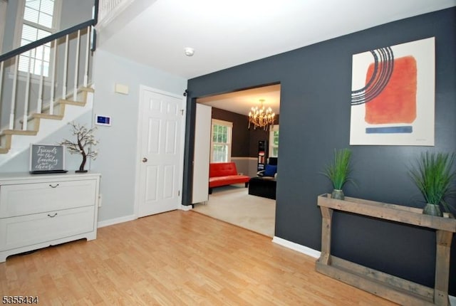entrance foyer with light wood finished floors, a chandelier, stairs, and baseboards