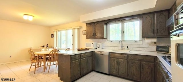 kitchen featuring stainless steel dishwasher, a sink, white microwave, dark brown cabinets, and a peninsula