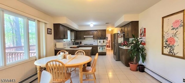 kitchen featuring a baseboard heating unit, dark brown cabinets, white appliances, under cabinet range hood, and light tile patterned floors