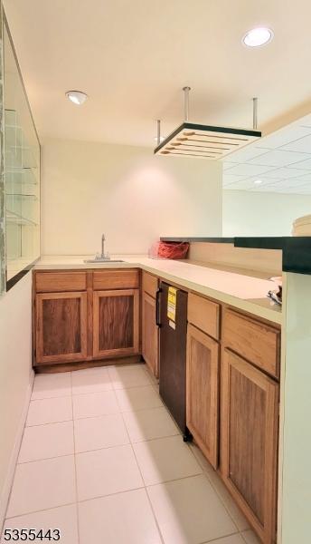 kitchen with a sink, light tile patterned flooring, light countertops, recessed lighting, and brown cabinetry