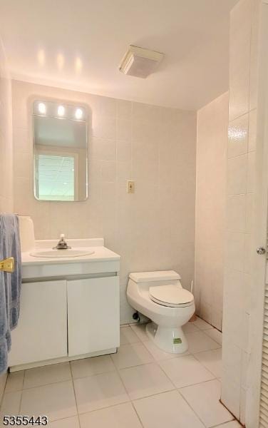 bathroom with toilet, tile patterned flooring, vanity, and tile walls