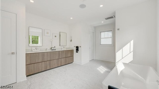 bathroom with double vanity, a freestanding bath, recessed lighting, and baseboards