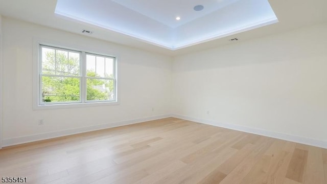 empty room featuring a raised ceiling, light wood-type flooring, and baseboards