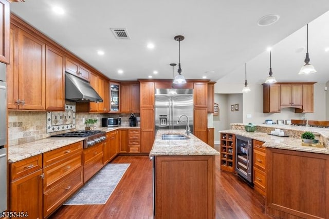 kitchen featuring beverage cooler, an island with sink, under cabinet range hood, a sink, and stainless steel appliances