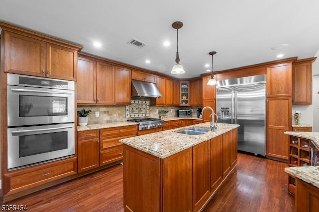 kitchen featuring brown cabinetry, visible vents, appliances with stainless steel finishes, a sink, and under cabinet range hood