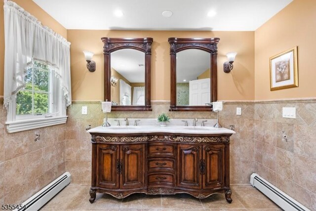 bathroom with tile walls, a baseboard heating unit, wainscoting, and a sink