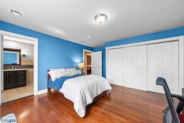bedroom featuring baseboards, wood finished floors, ensuite bathroom, visible vents, and a closet