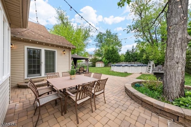 view of patio / terrace featuring outdoor dining area, a shed, and a covered pool